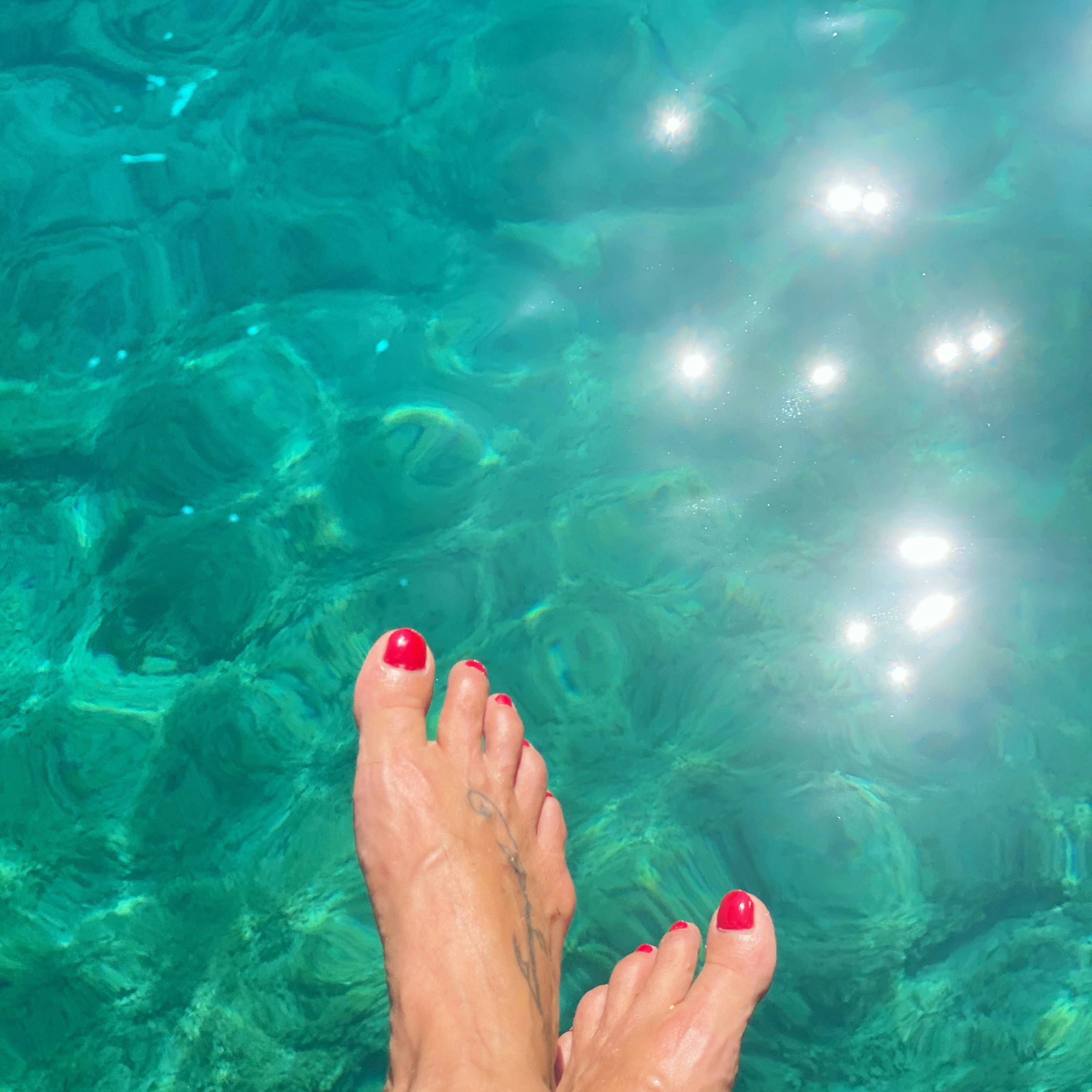 A woman's feet in the water with red nail polish
