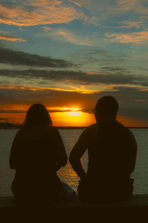 A man and a woman sitting on a bench watching the sunset