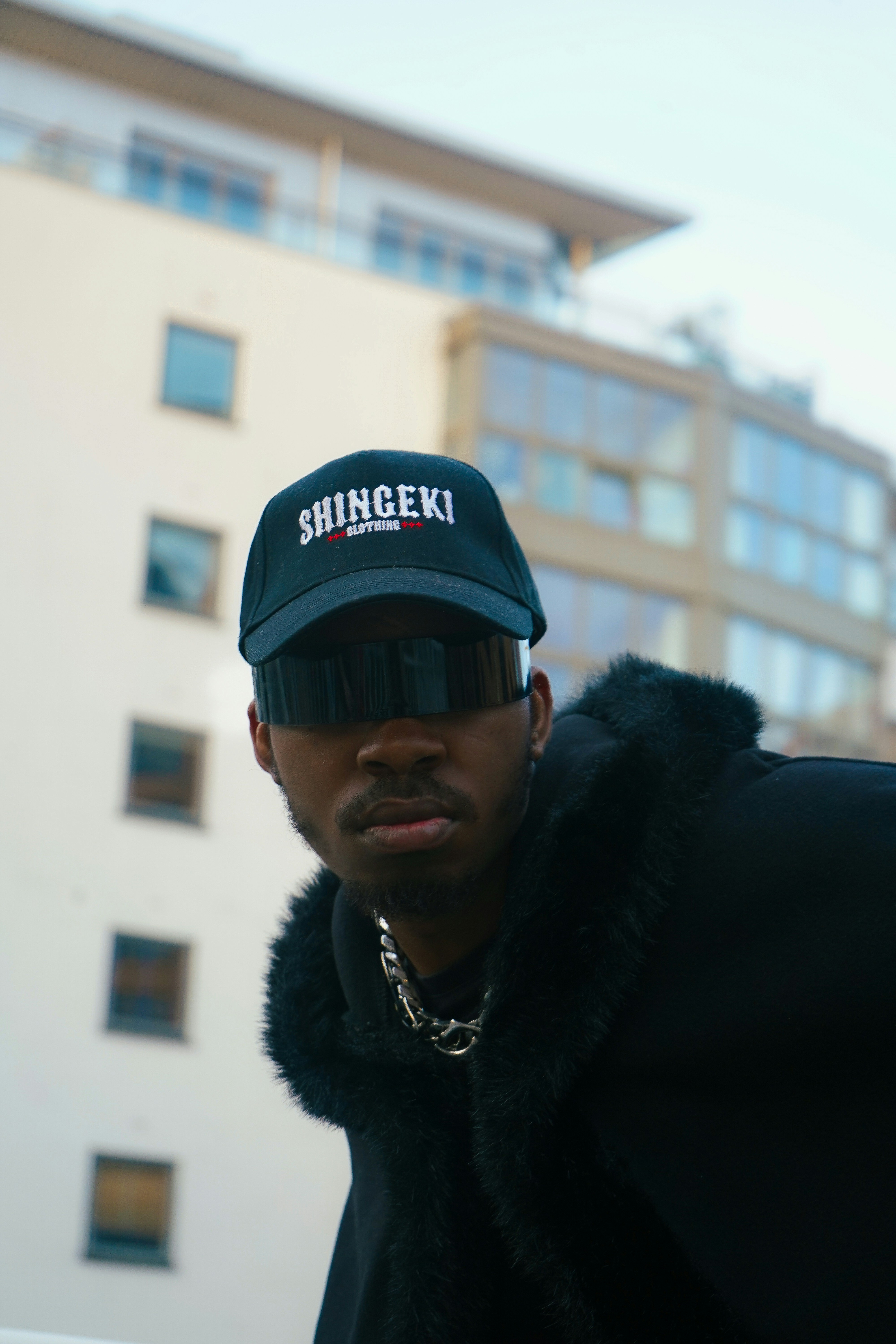 A man in a black coat and hat standing in front of a building