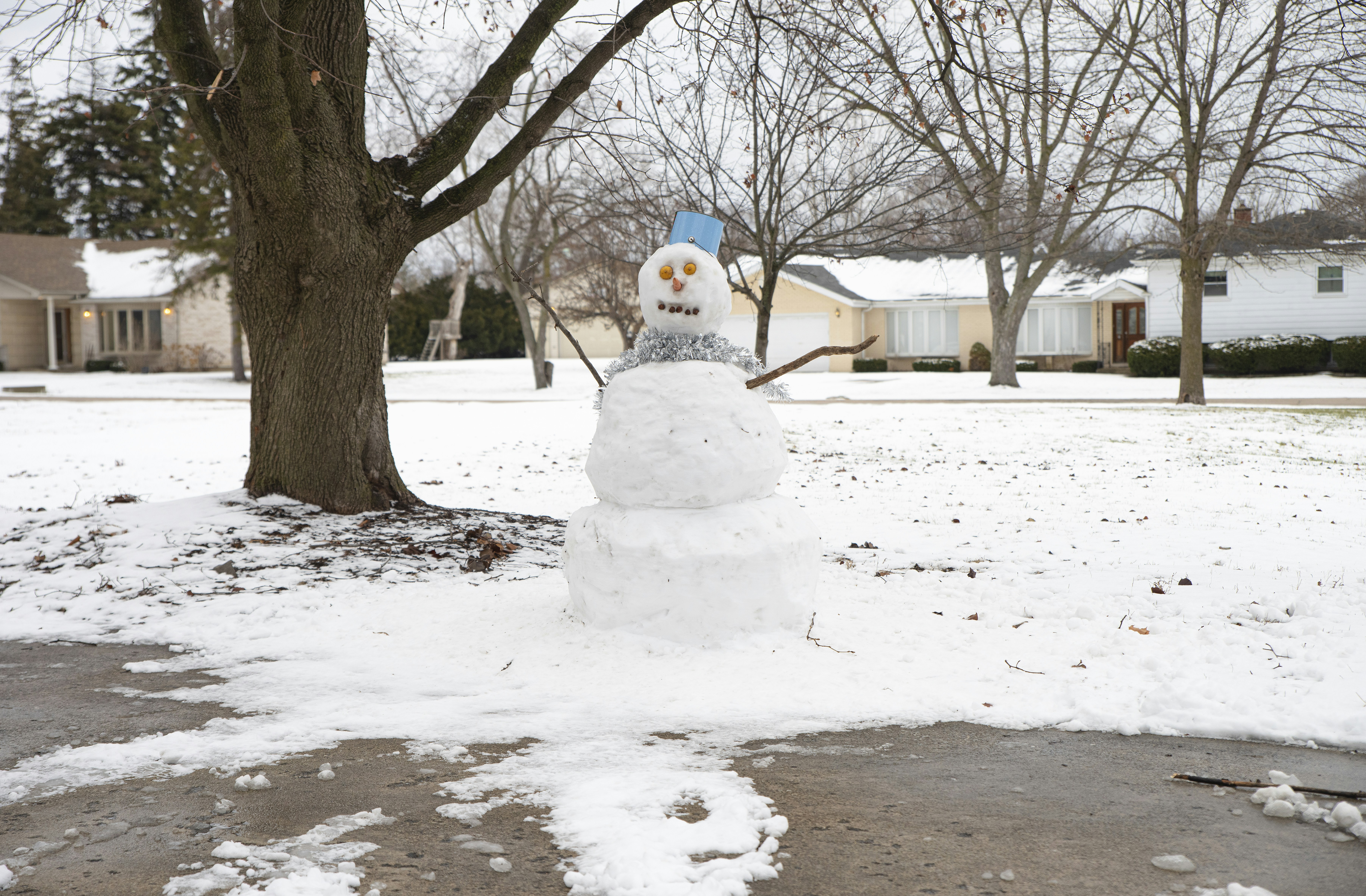 A snowman is standing in the middle of a driveway