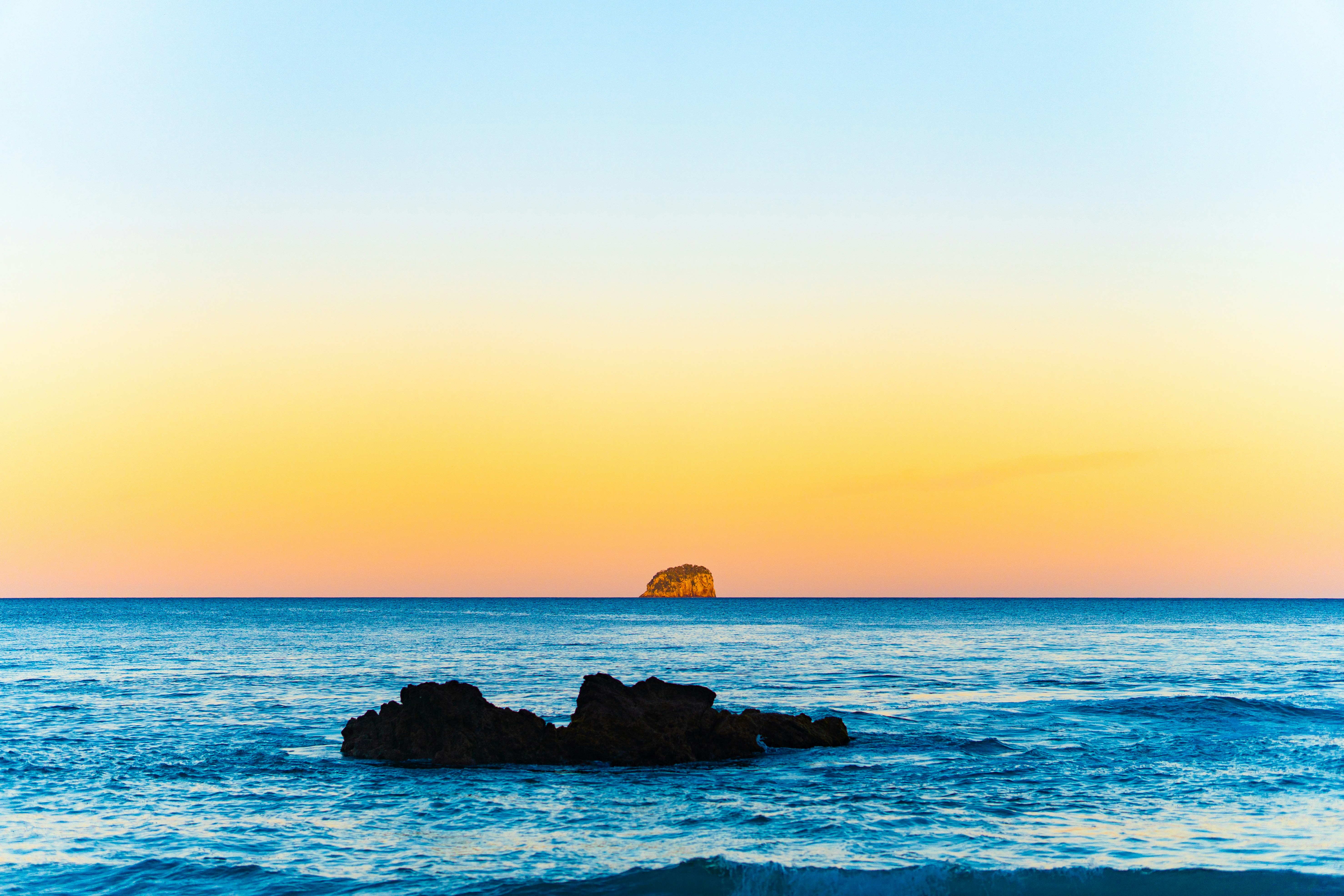 The sun is setting over the ocean with a rock in the foreground