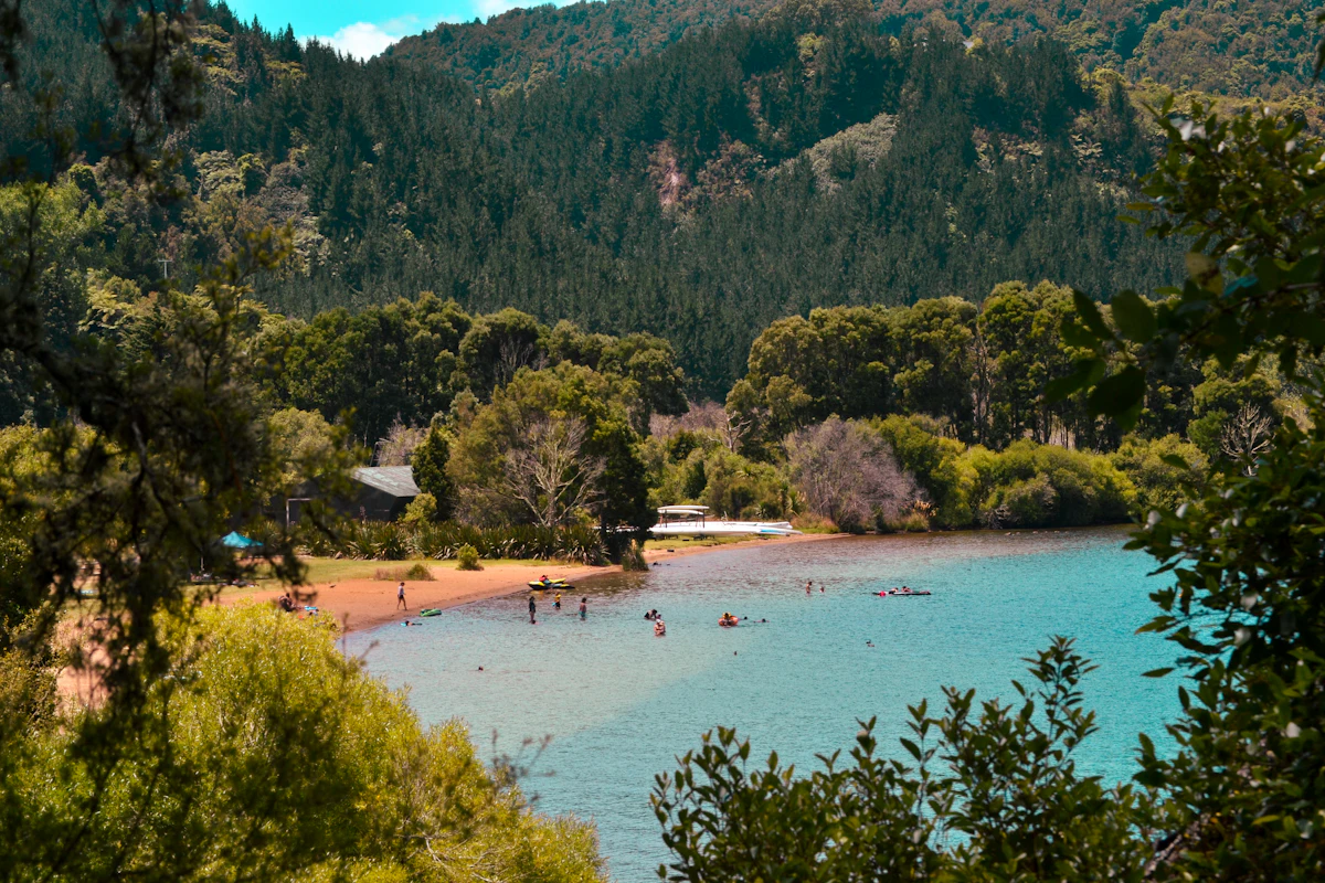 Swimmers and kayaks at a small beach on Lake Ōkareka, below steep forested hills