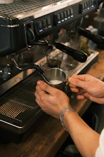 A person is holding a coffee cup in front of an espresso machine