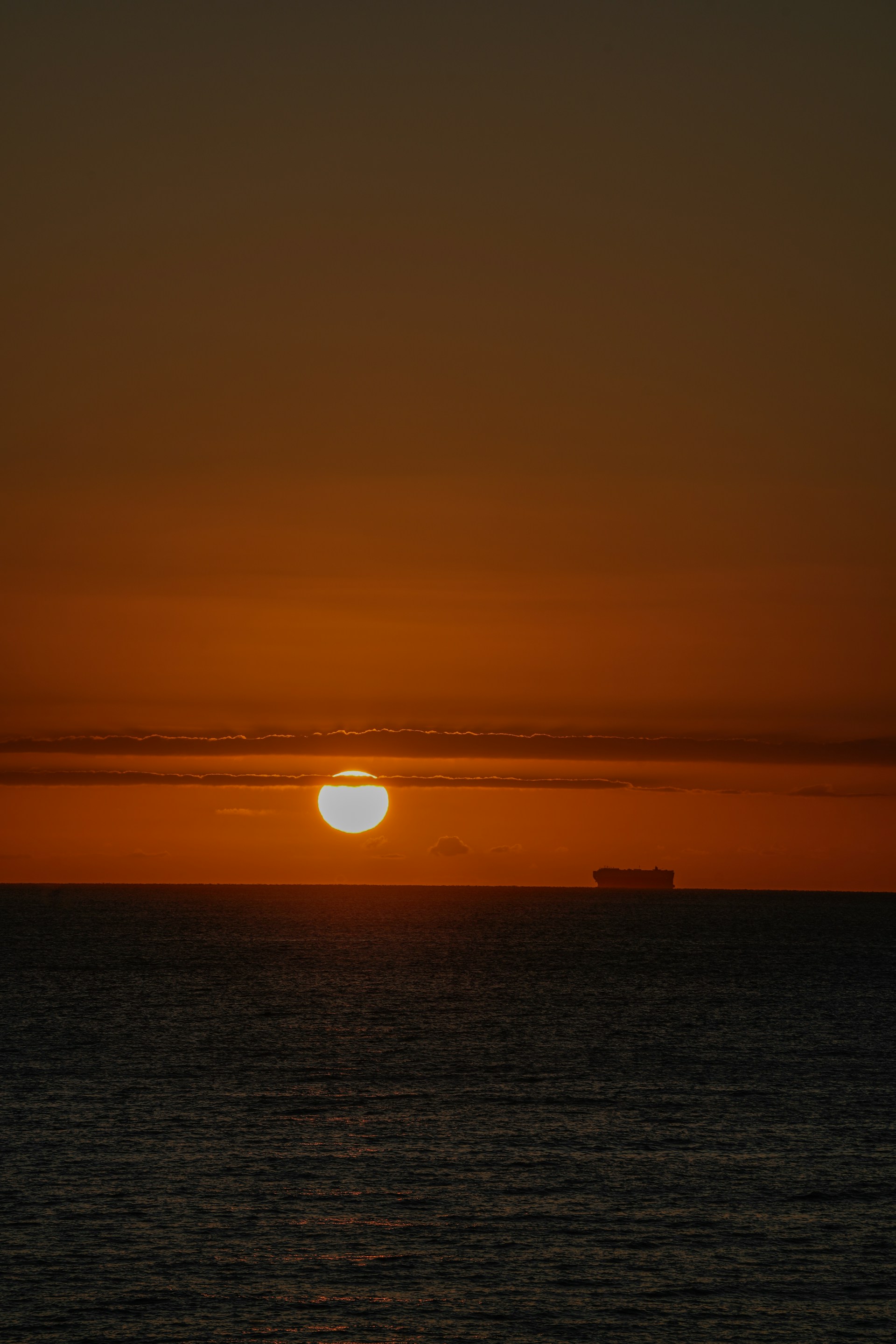 The sun is setting over the ocean with a boat in the distance