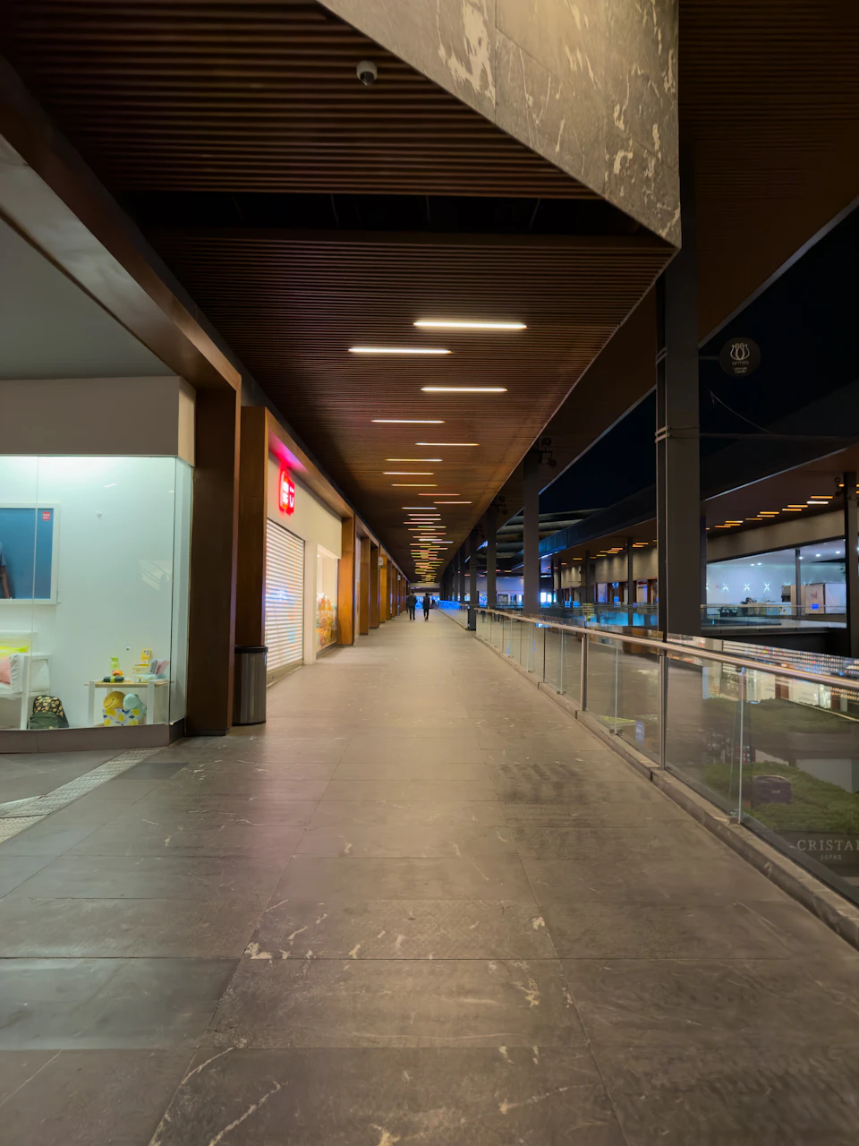Long, narrow hallway with wooden ceiling and gray tile floor features two shops nearby