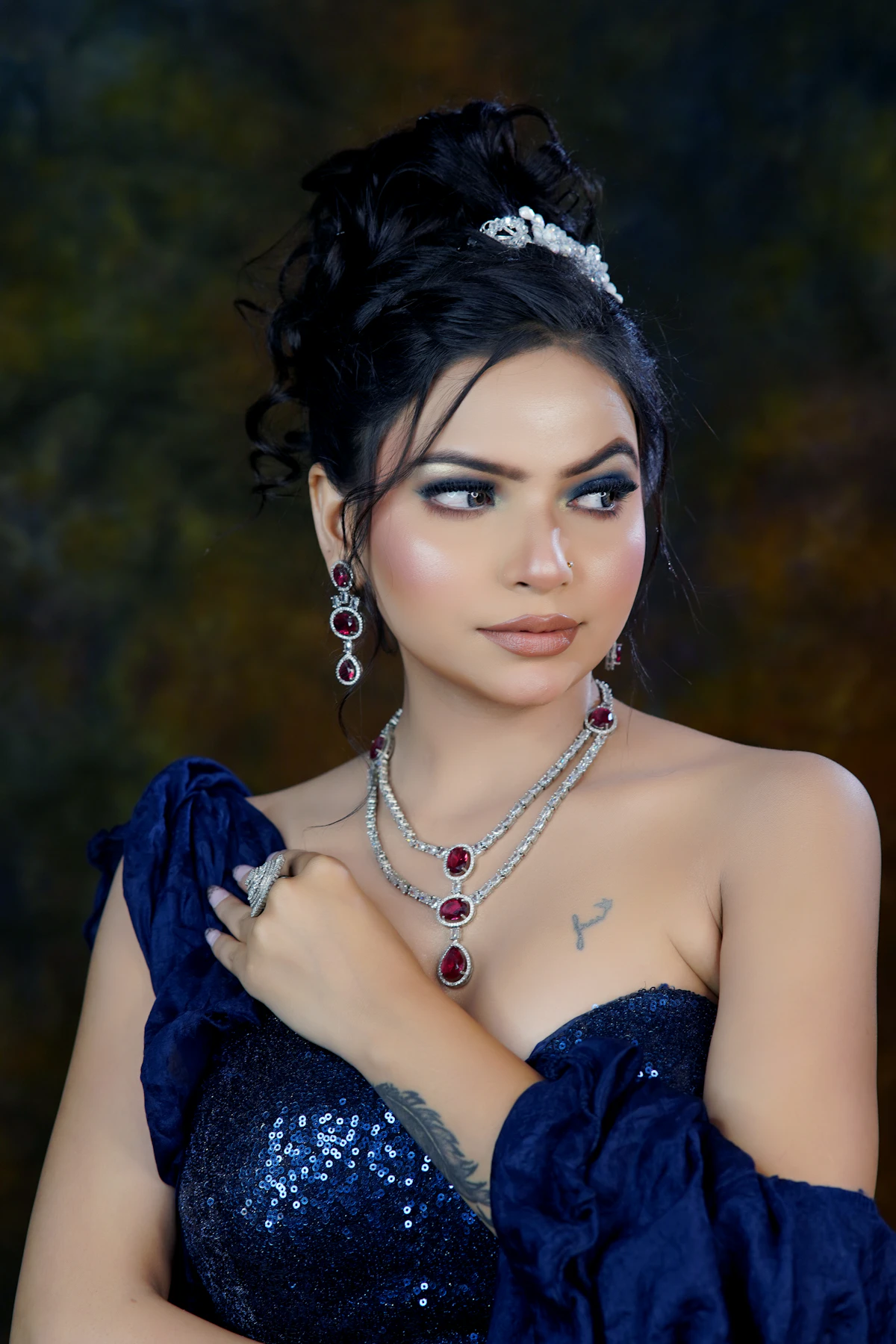 Adult woman in a midnight blue gown wearing a ruby and diamond necklace, drop earrings and a cocktail ring