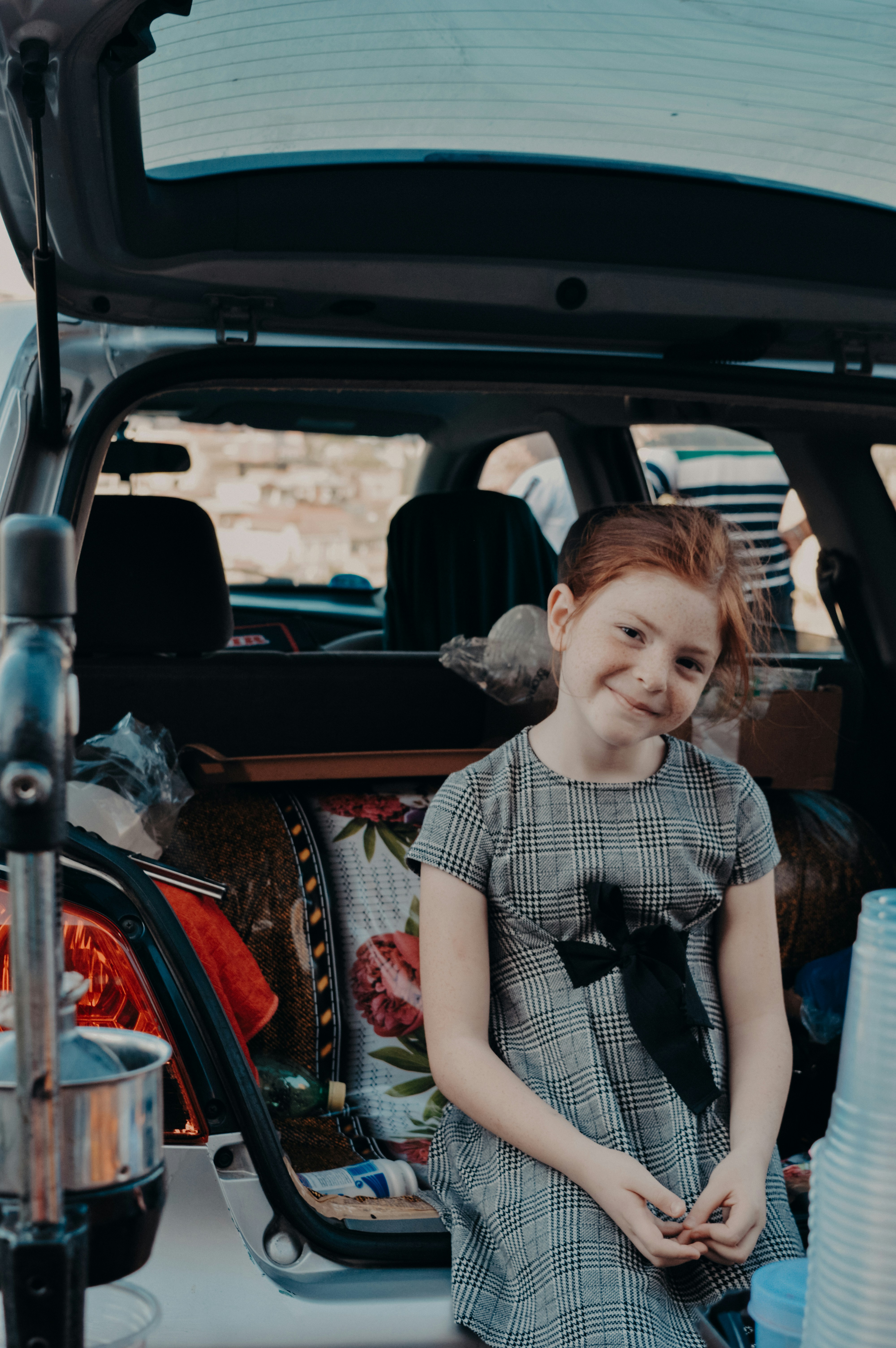 A little girl standing in the trunk of a car