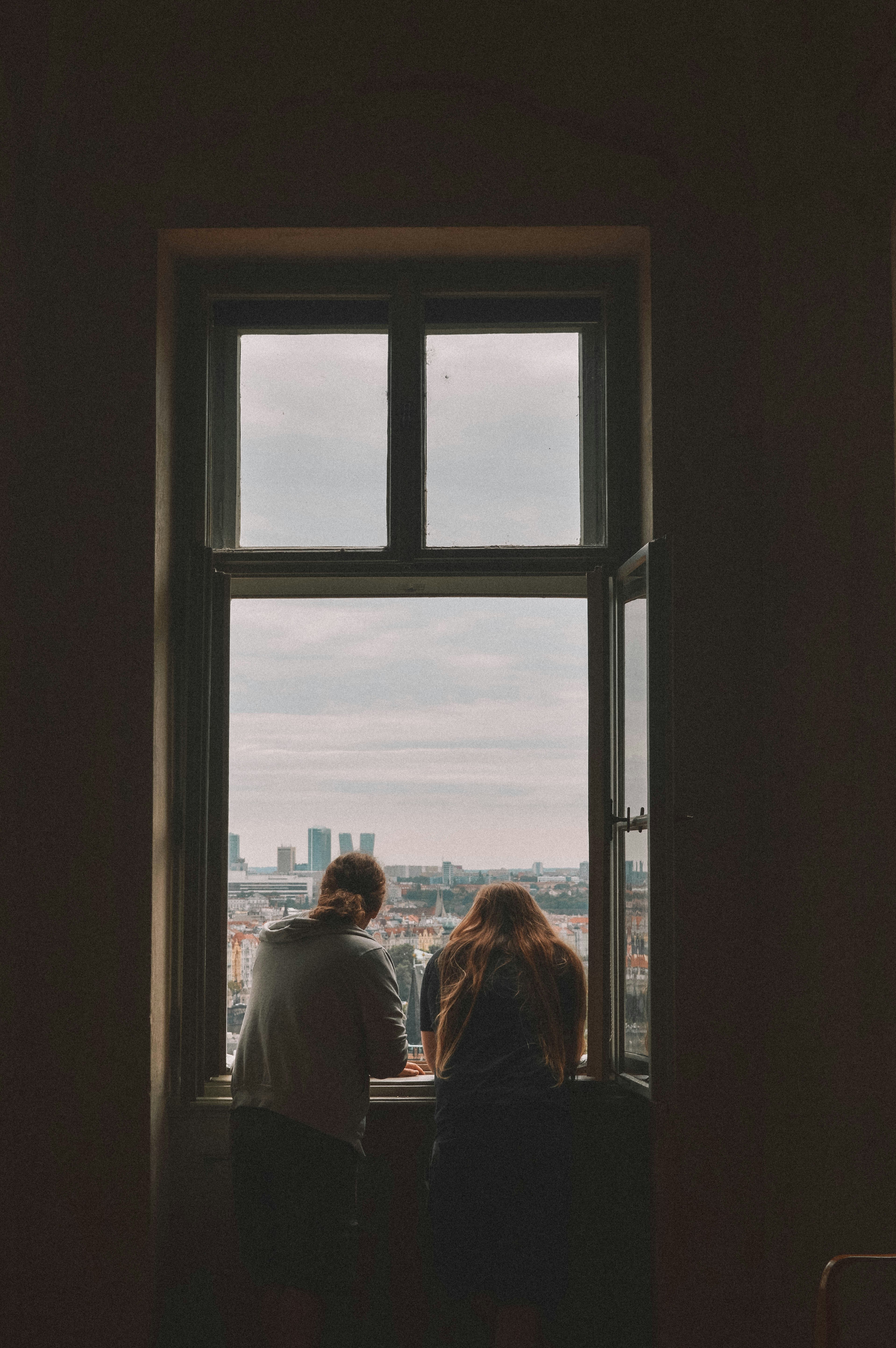 Two people sitting on a window sill looking out at the city