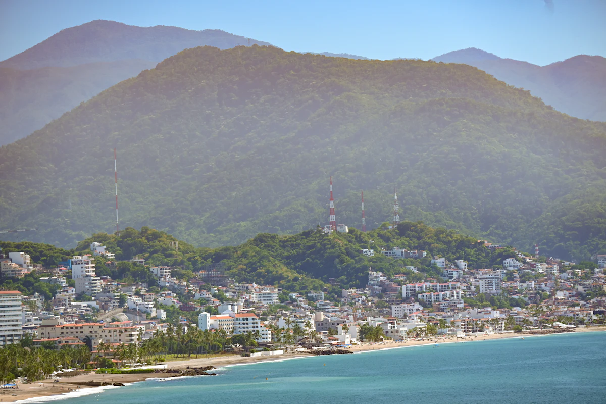 A beach and hillside neighborhoods in Puerto Vallarta below a forested mountain
