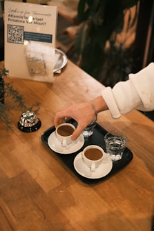 A person pouring coffee into two cups on a table