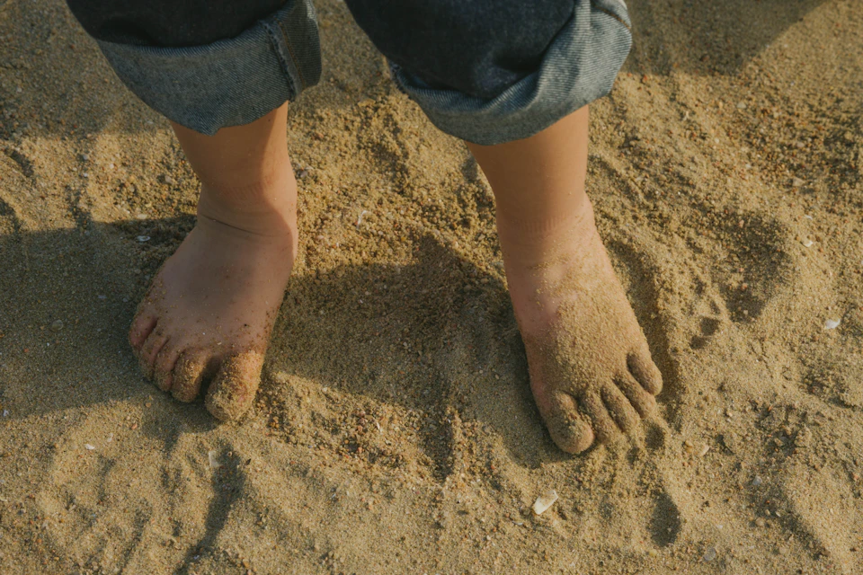 Person stands on sandy beach with feet pointing in opposite directions on warm sand