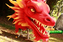A red dragon statue sitting on top of a lush green field