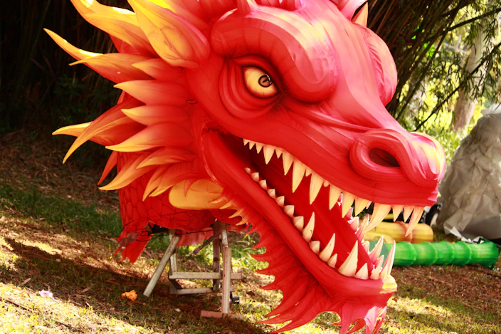 A red dragon statue sitting on top of a lush green field