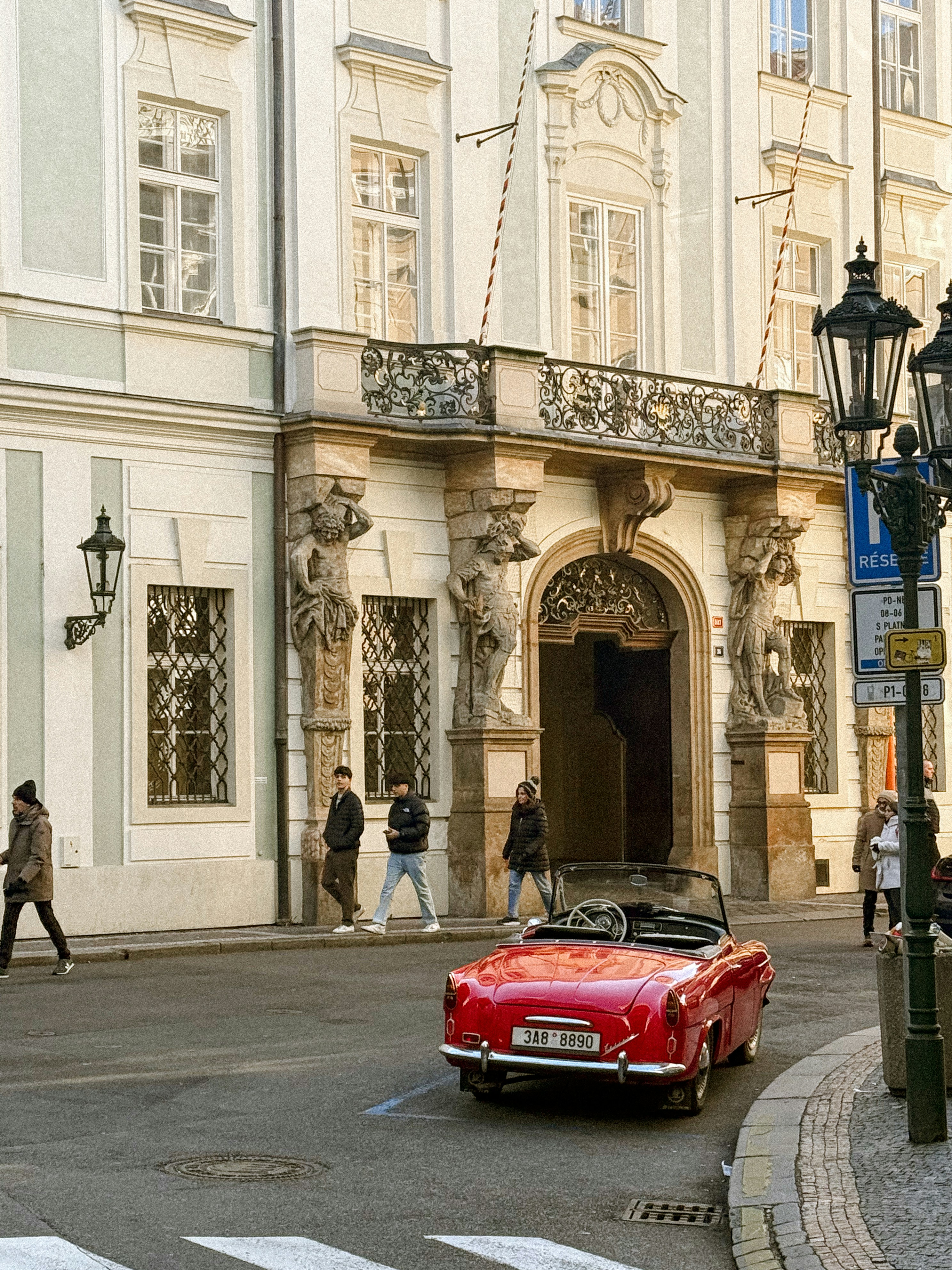 A red car driving down a street next to a tall building