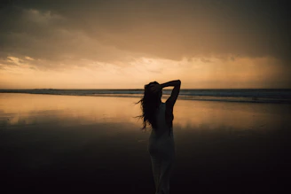 A woman standing on a beach with her arms in the air