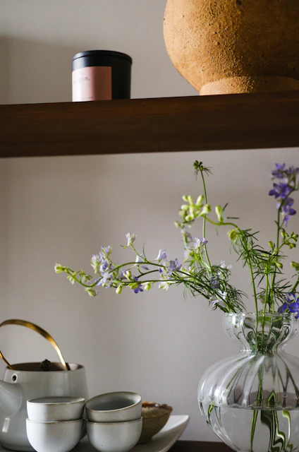 A shelf with a vase of flowers and a tea pot