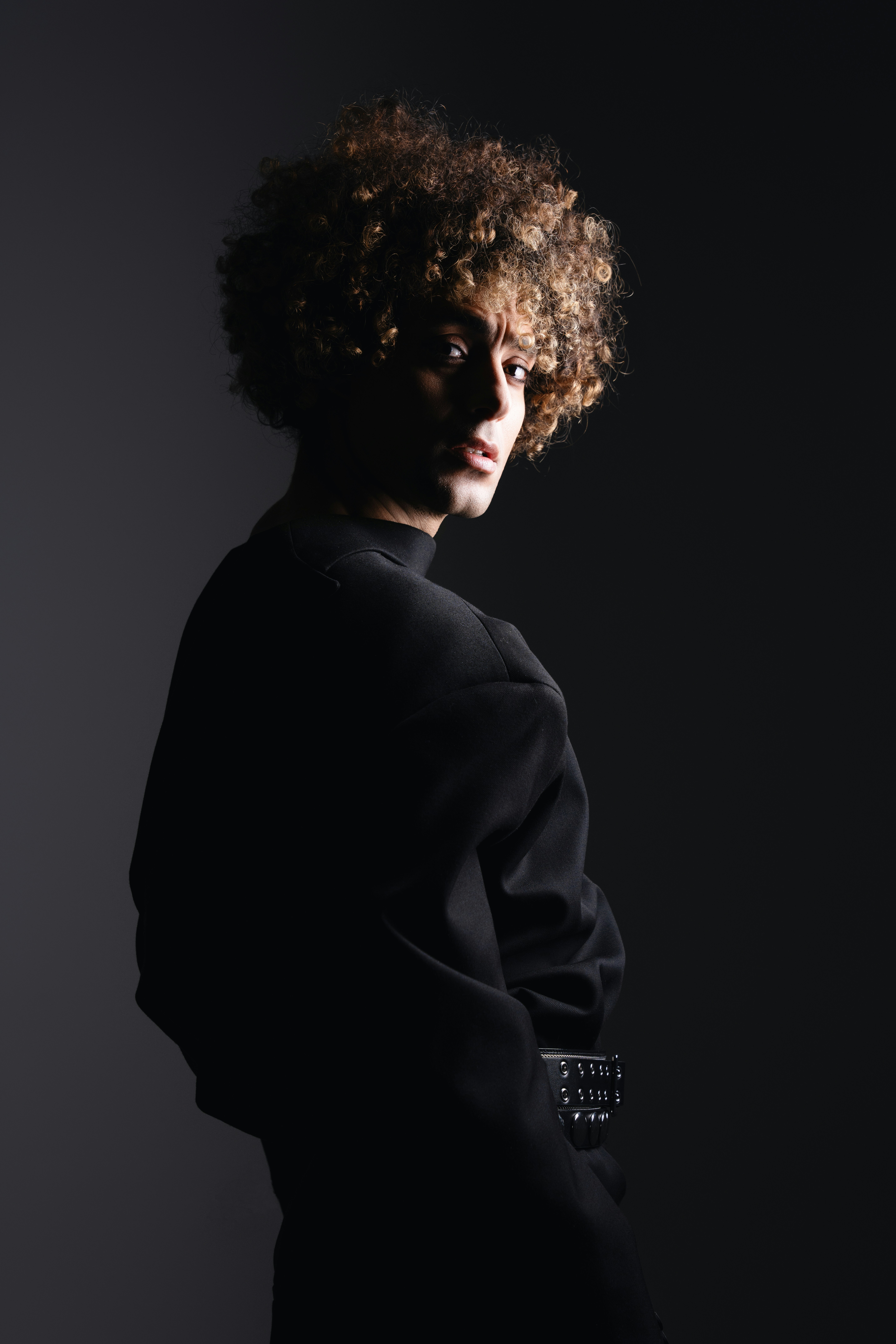 A man with curly hair standing in a dark room