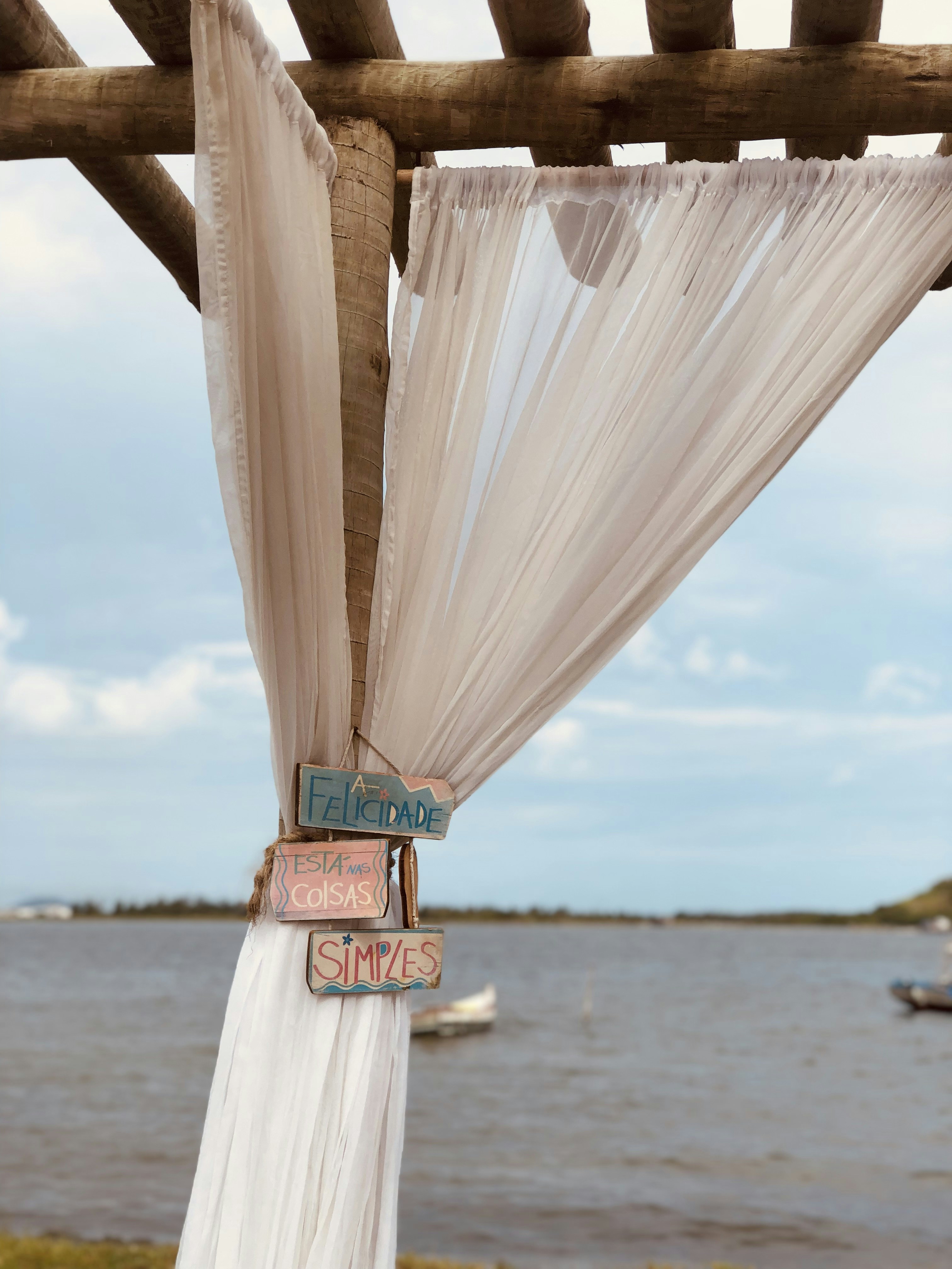 Wooden pergola with sheer curtains stands beside a calm lake.