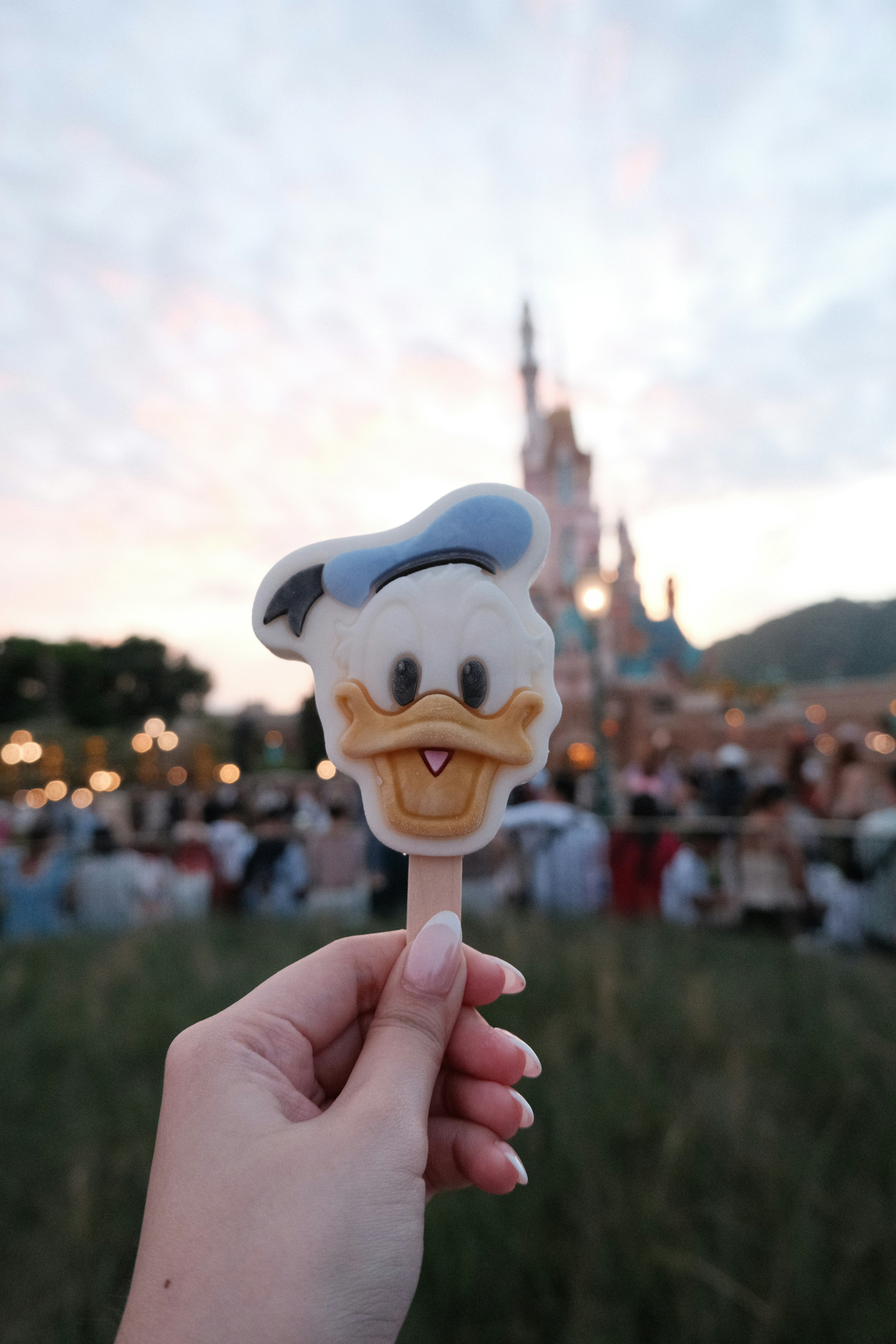 Una mano sosteniendo una piruleta de Mickey Mouse frente a un castillo