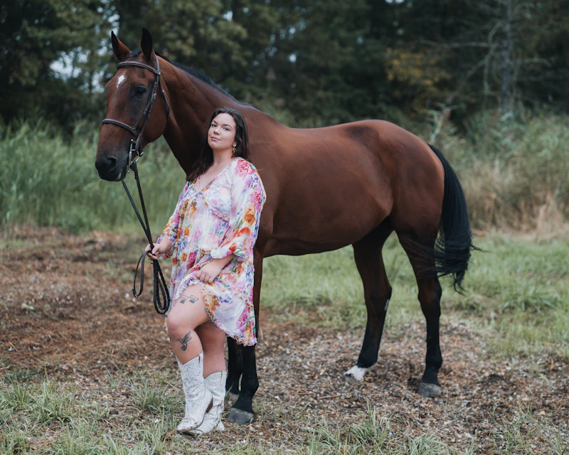 confident curvy woman standing beside a brown horse