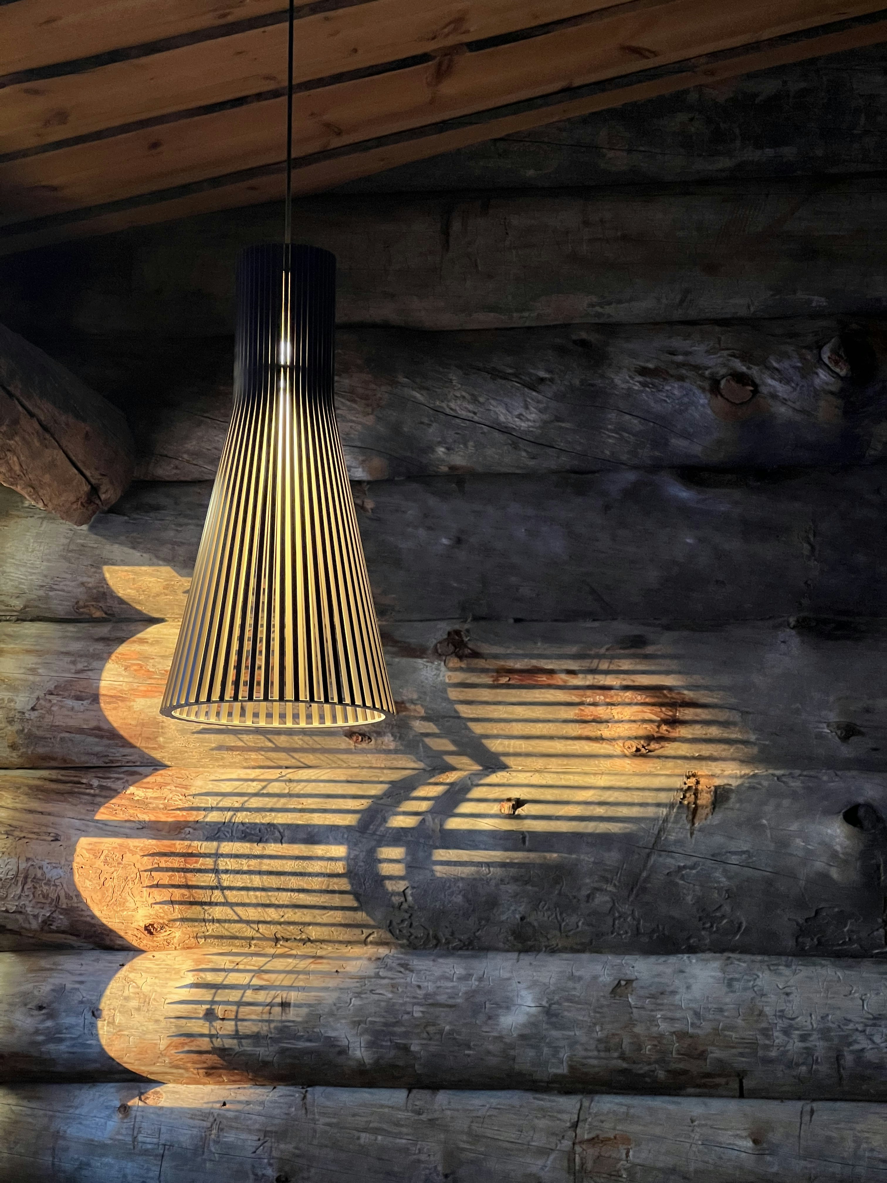 A lamp hanging from a wooden ceiling next to logs