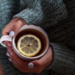 A woman holding a cup of tea with a lemon slice in it