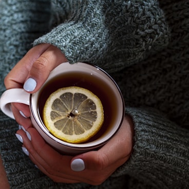 A woman holding a cup of tea with a lemon slice in it