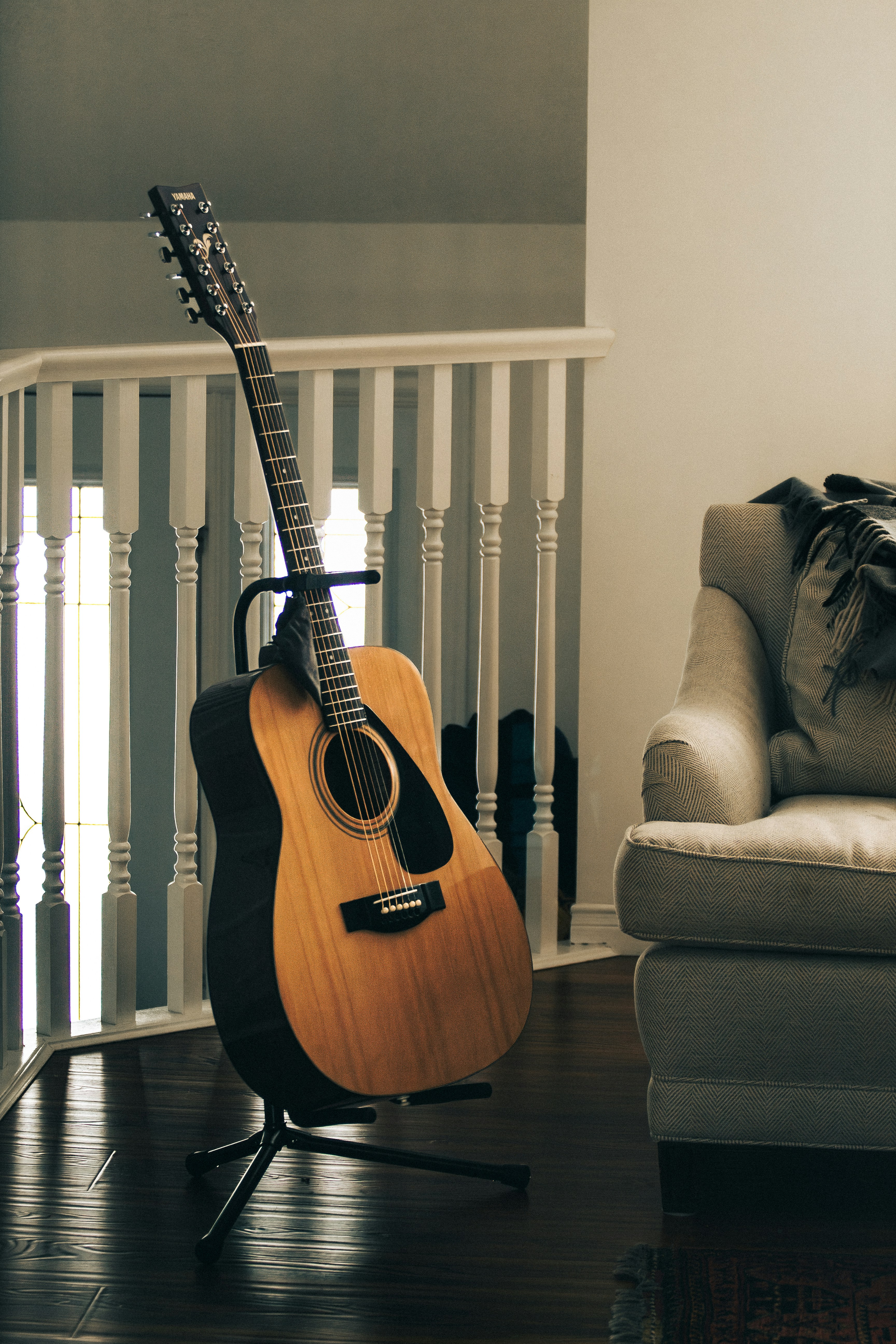 Twelve-string acoustic guitar standing on a tripod near an armchair.