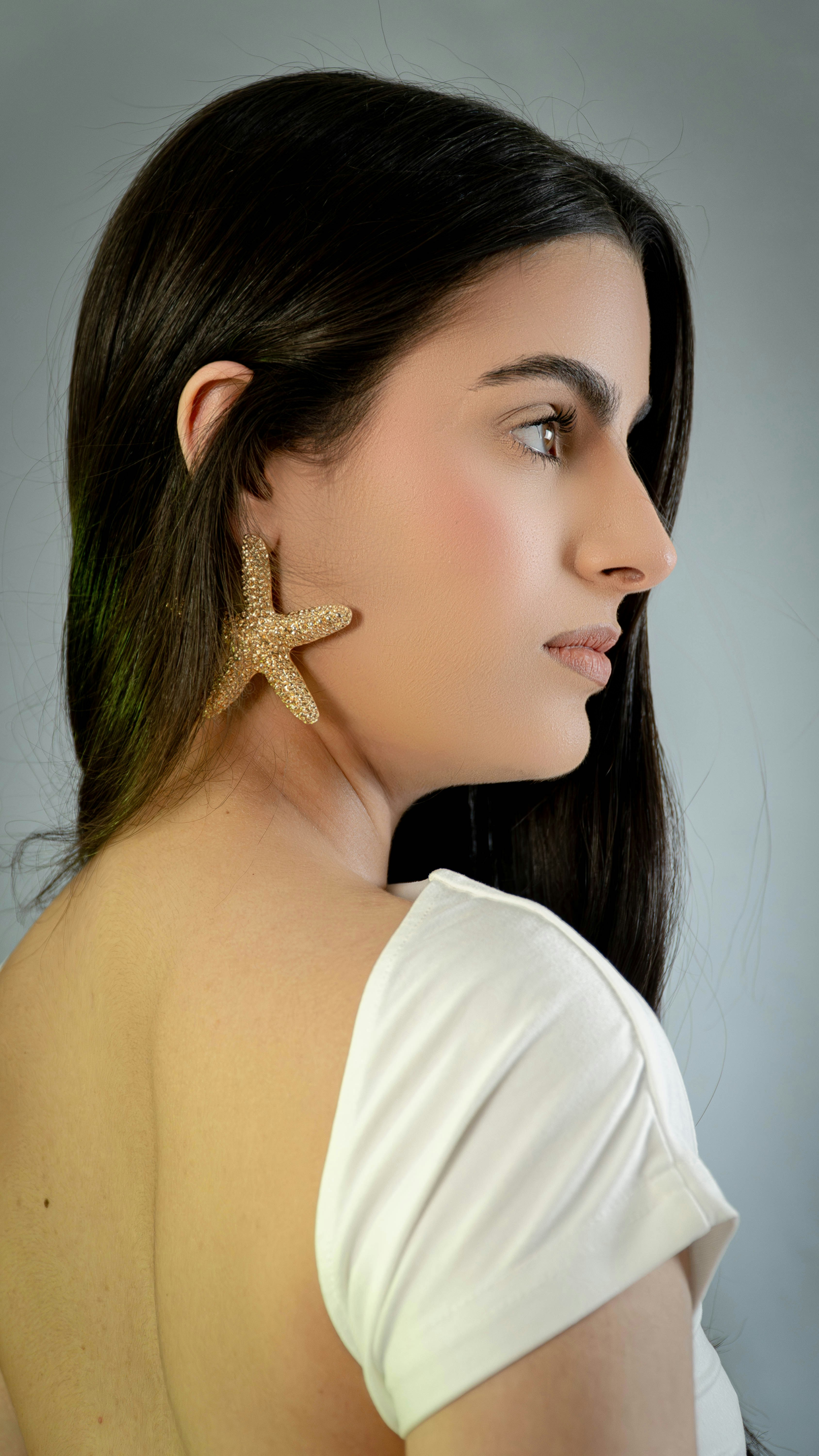 Una mujer con un top blanco con un pendiente de estrella de mar