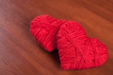Two red yarn hearts on a wooden surface