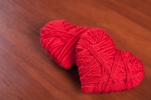 Two red yarn hearts on a wooden surface