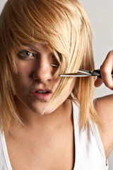 A woman cutting her hair with a pair of scissors