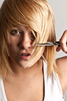 A woman cutting her hair with a pair of scissors
