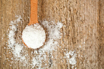 A wooden spoon filled with sugar on top of a table