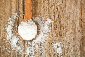 A wooden spoon filled with sugar on top of a table