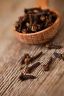 A wooden spoon filled with cloves on top of a wooden table