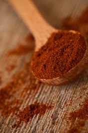 A wooden spoon filled with red powder on top of a wooden table