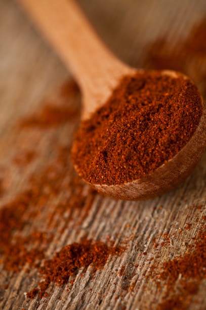A wooden spoon filled with red powder on top of a wooden table