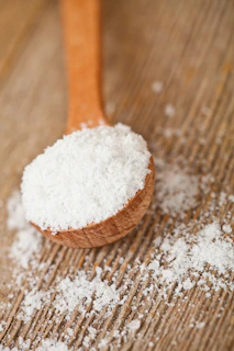A wooden spoon filled with sugar on top of a wooden table
