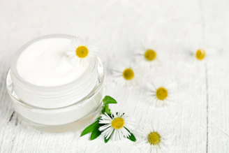 A jar of cream with daisies on a white wooden table