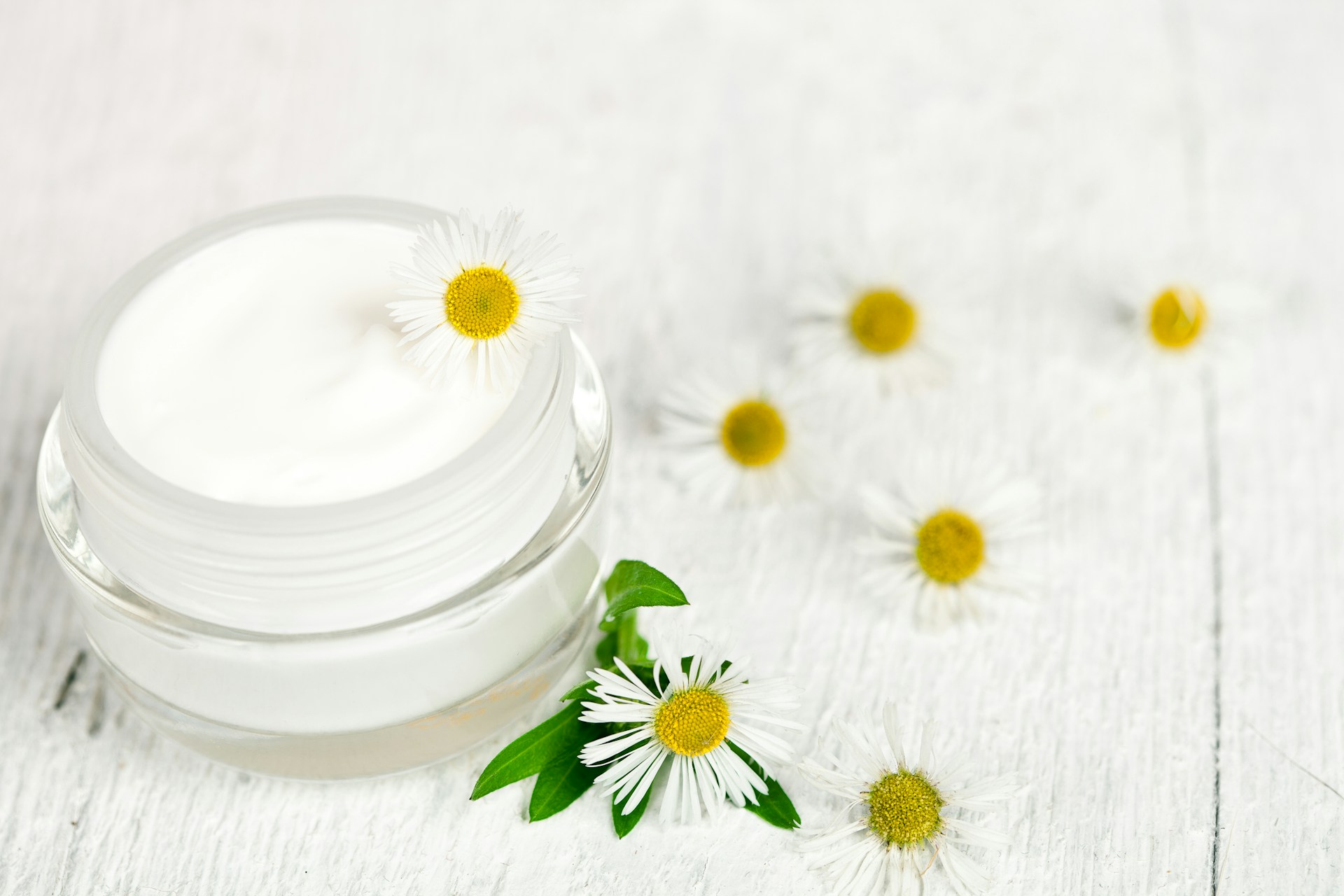 A jar of cream with daisies on a white wooden table