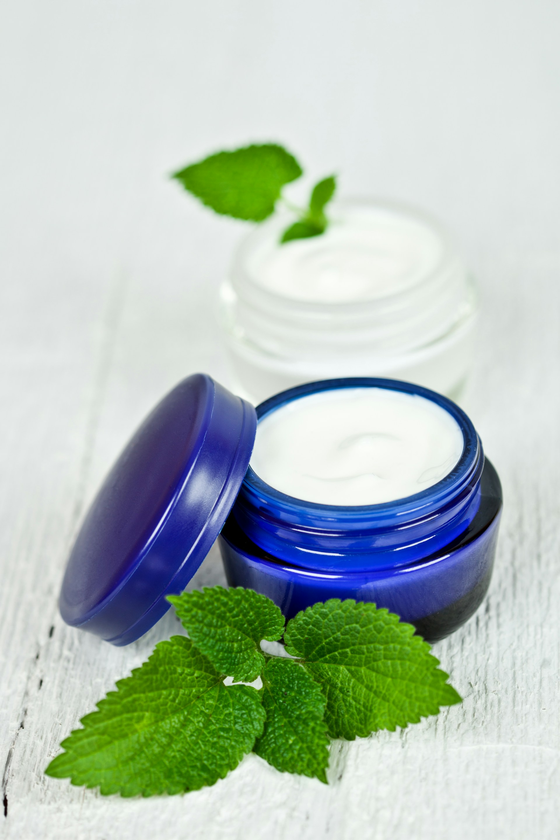 A jar of cream and a green leaf on a white surface