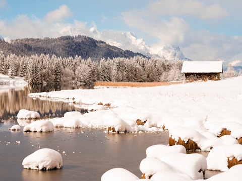 A snowy landscape with a small pond and mountains in the background