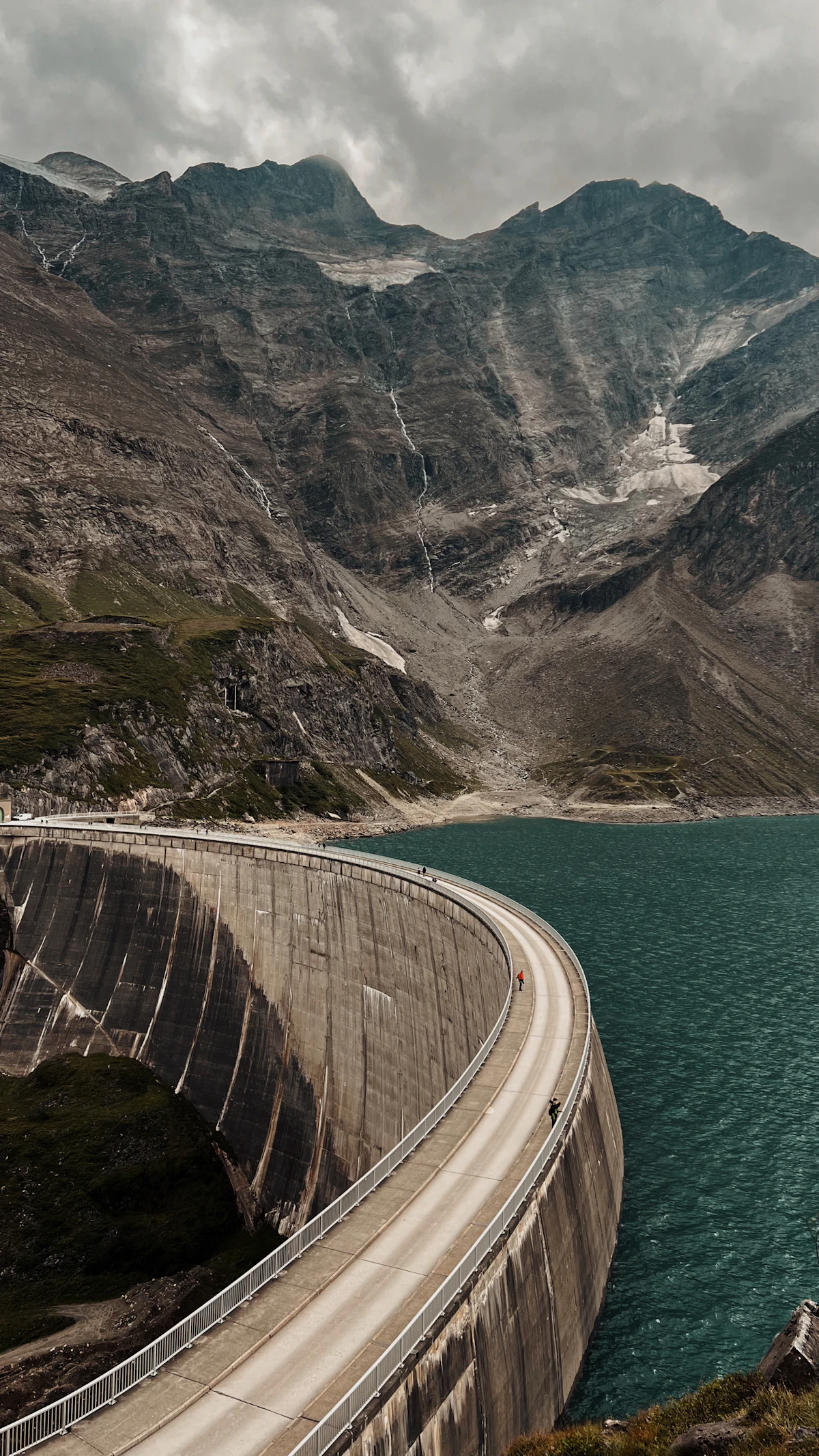 The curved wall of the Mooserboden dam above Kaprun, with rock walls and snow patches behind the reservoir