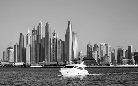 Black-and-white photograph of a motor yacht passing the Dubai Marina skyline