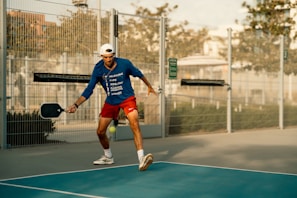 A man in blue shirt and red shorts playing a game of tennis