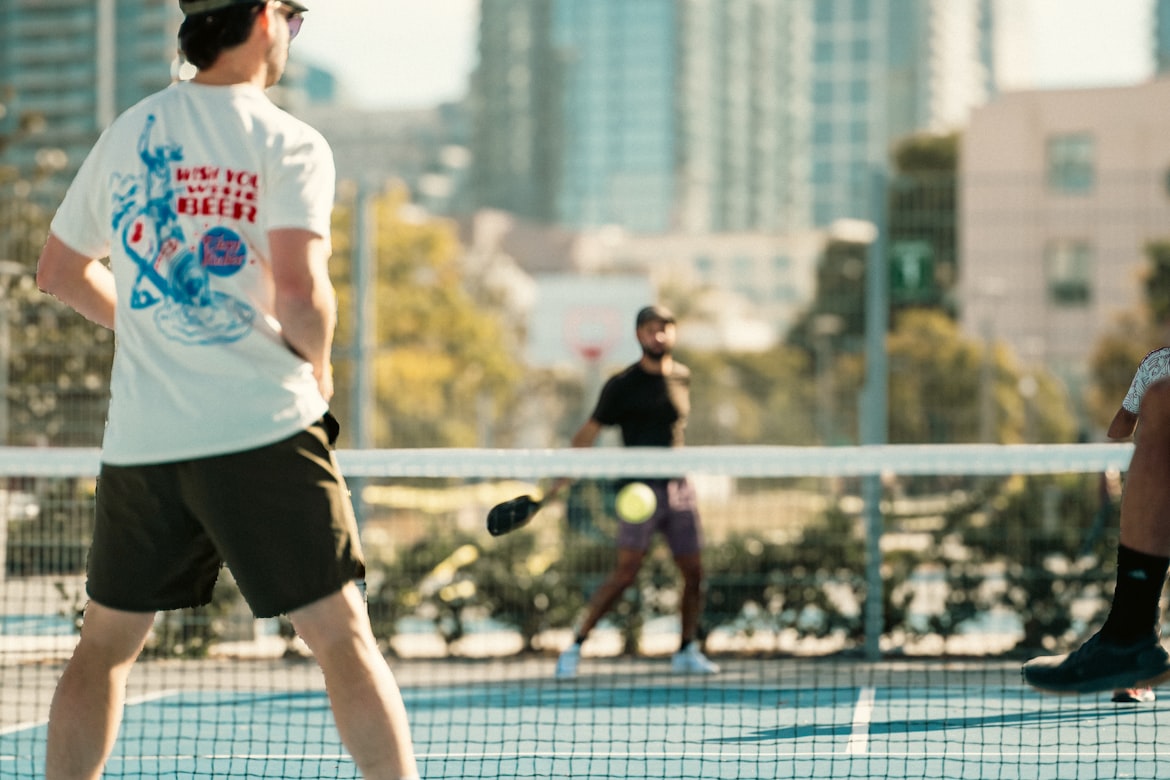Young children learning to play tennis on a community court with a coach demonstrating a forehand swing