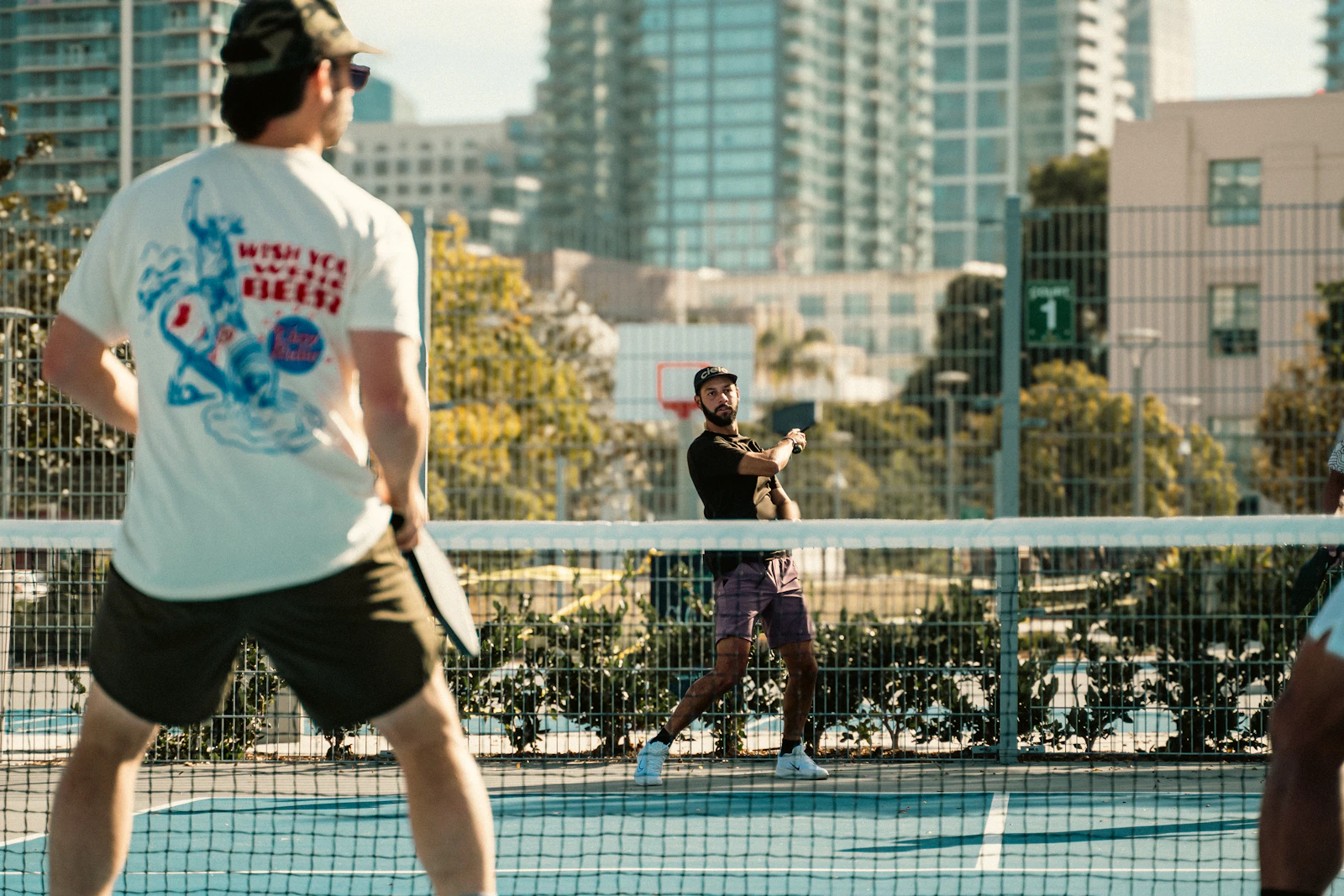 Adults playing a doubles rally on an outdoor pickleball court.