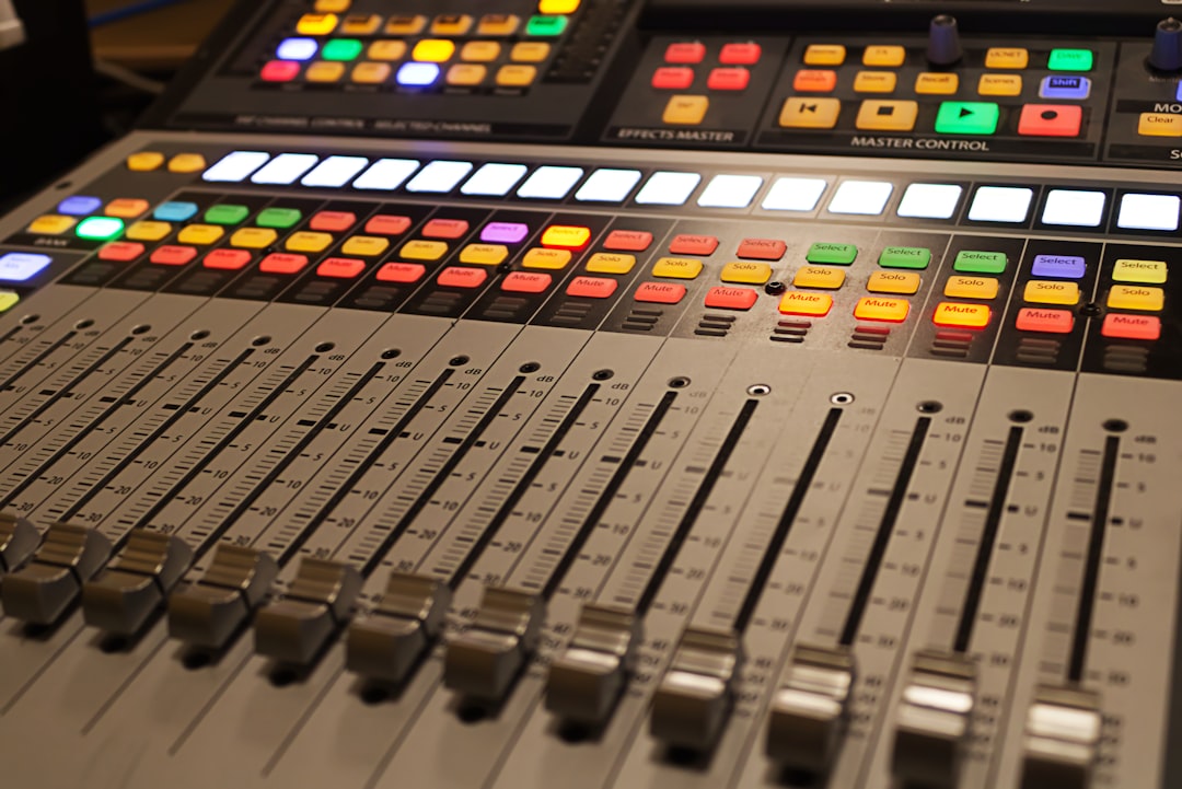 A sound board with many different colored buttons, An audio mixing console in dramatic lighting and a soft focus.