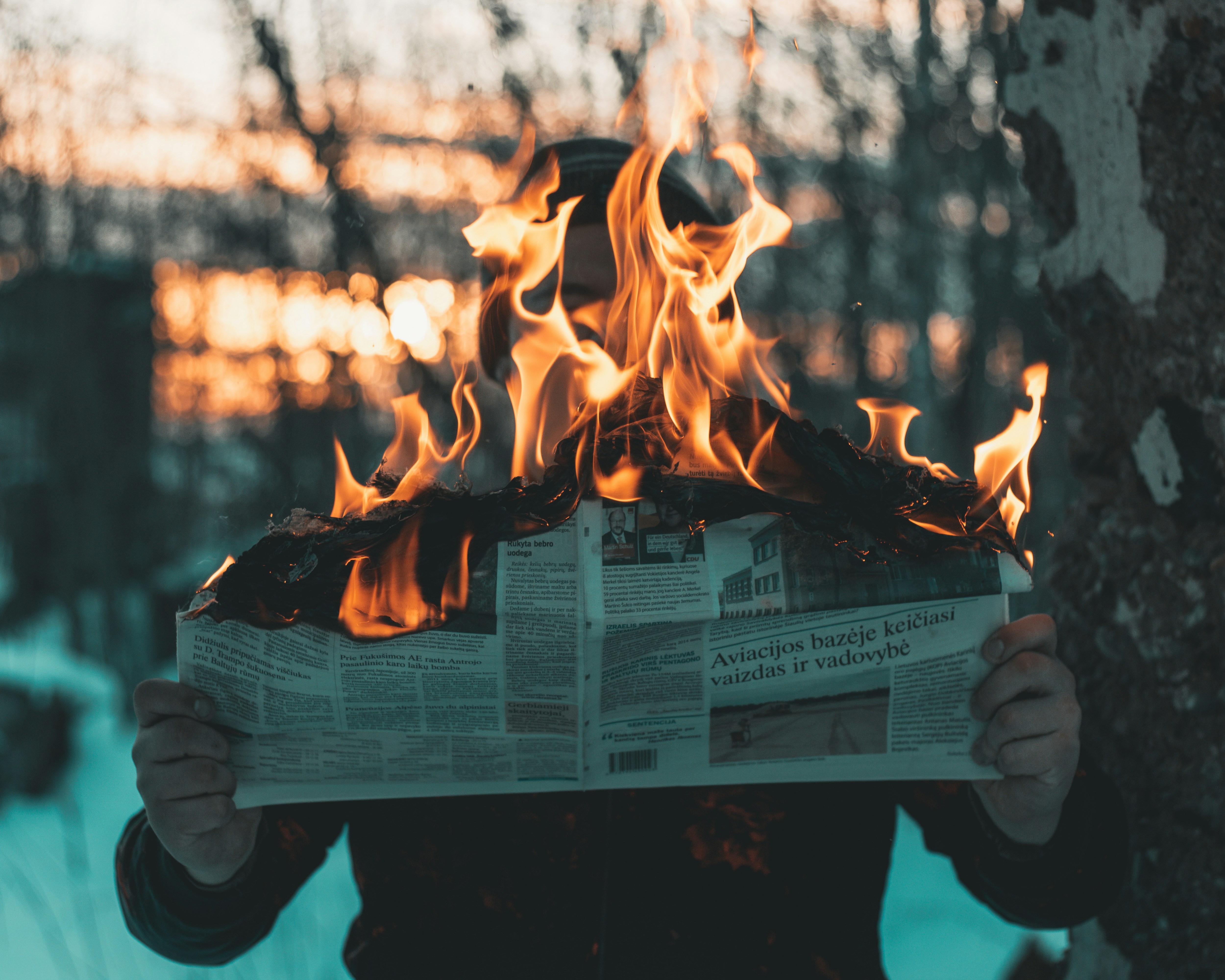 A person holding a newspaper in front of a fire